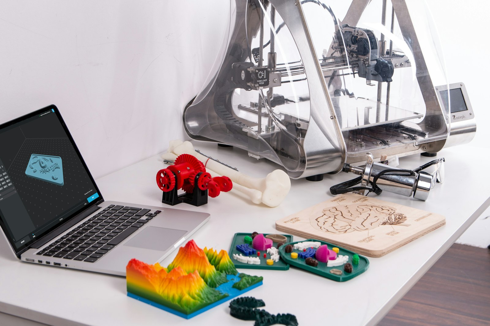Laptop met 3D-model naast een 3D-printer en geprinte prototypes